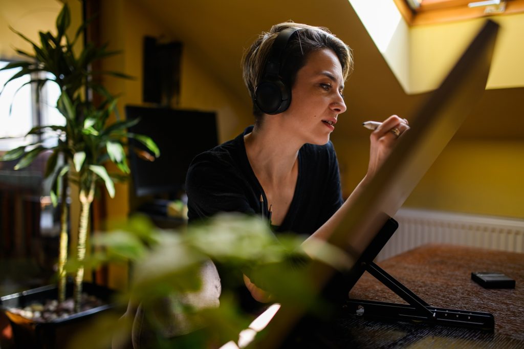 Artistic illustrator with headphones is pencil drawing on board at home